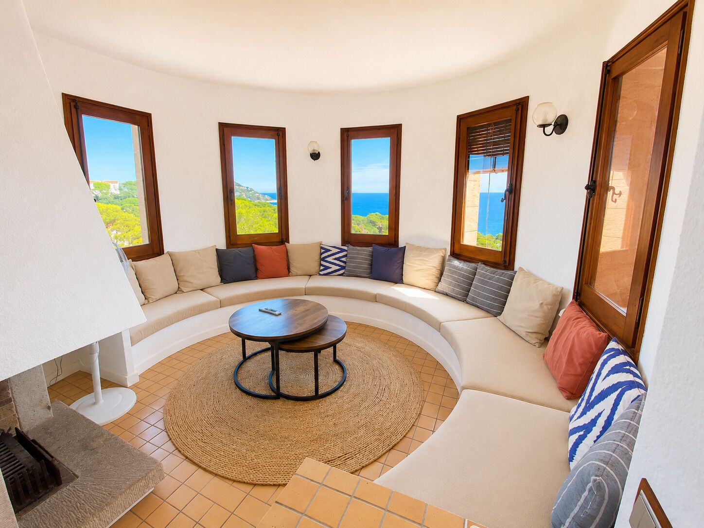 Sala de estar circular com um sofá, uma mesa de centro e vista para o mar através de grandes janelas.