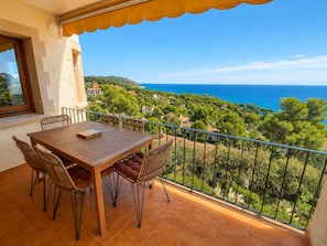 A balcony with a wooden table and chairs, overlooking a coastal landscape with houses and trees.