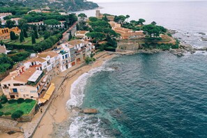 Vista aérea de uma vila costeira com edifícios ao longo da praia, uma torre imponente e costa rochosa.