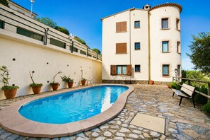 A swimming pool with a stone deck, surrounded by potted plants and a bench.