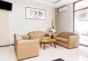 A modern living room with beige sofas, a glass coffee table, and a framed artwork on the wall. - Capital O 1867 Kara Guest House (Batam)