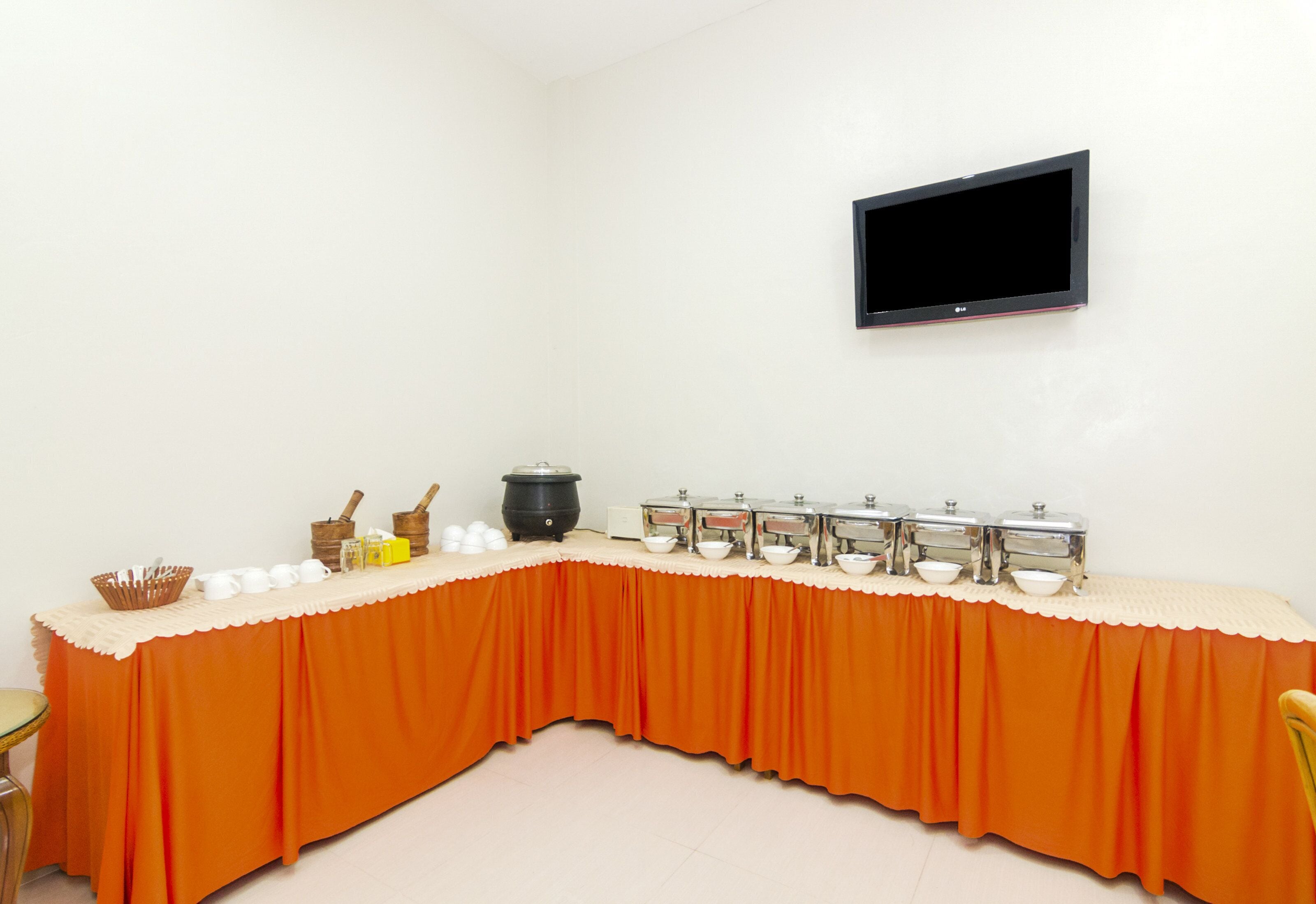 A conference room with a long table, a flat-screen TV mounted on the wall, and buffet-style food service.