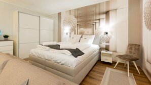A modern bedroom with a large bed, bedside tables, a chair, and decorative wall panels. - Budapest Downtown Residence (Budapest)