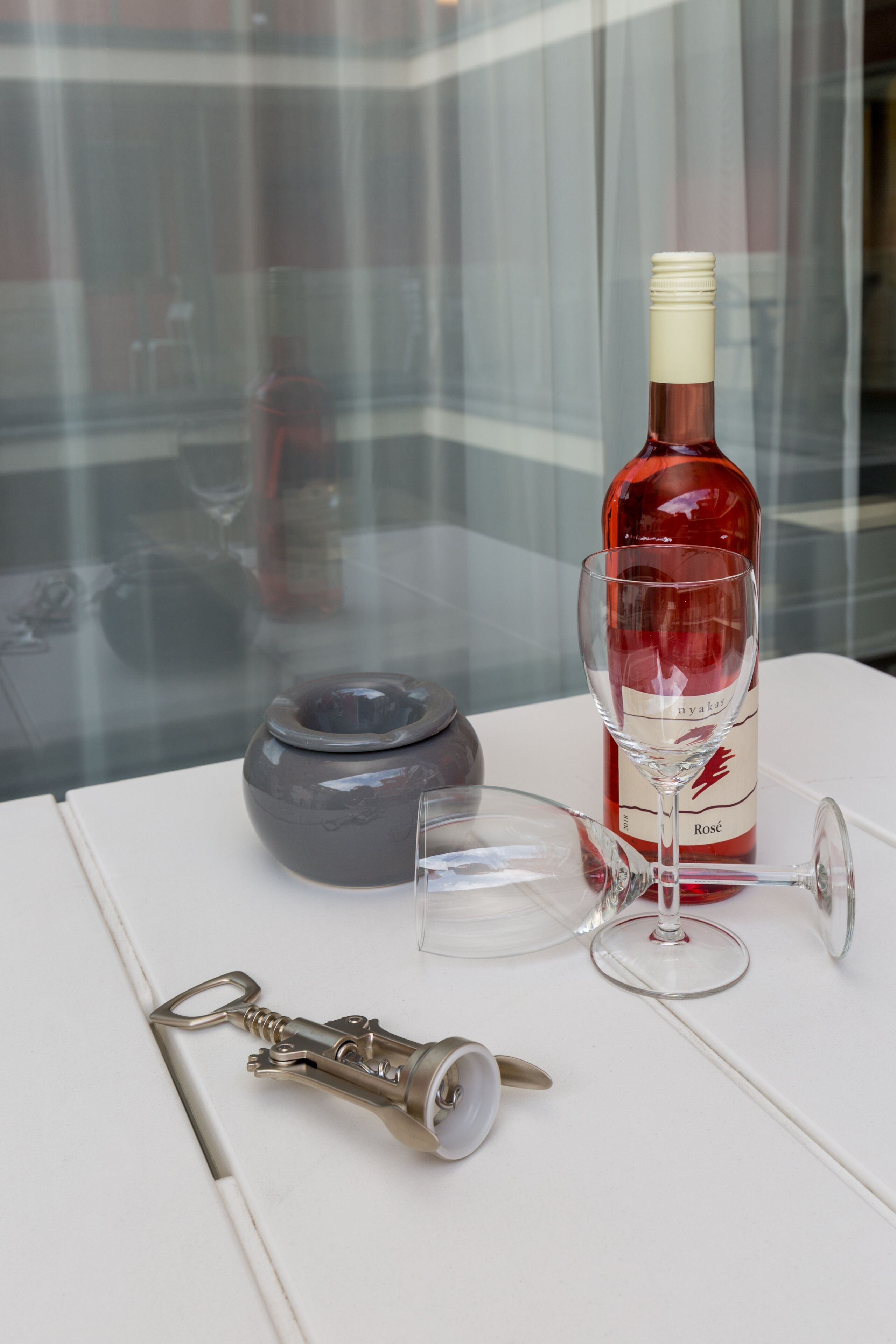 A bottle of wine, two wine glasses, and a key on a white table.