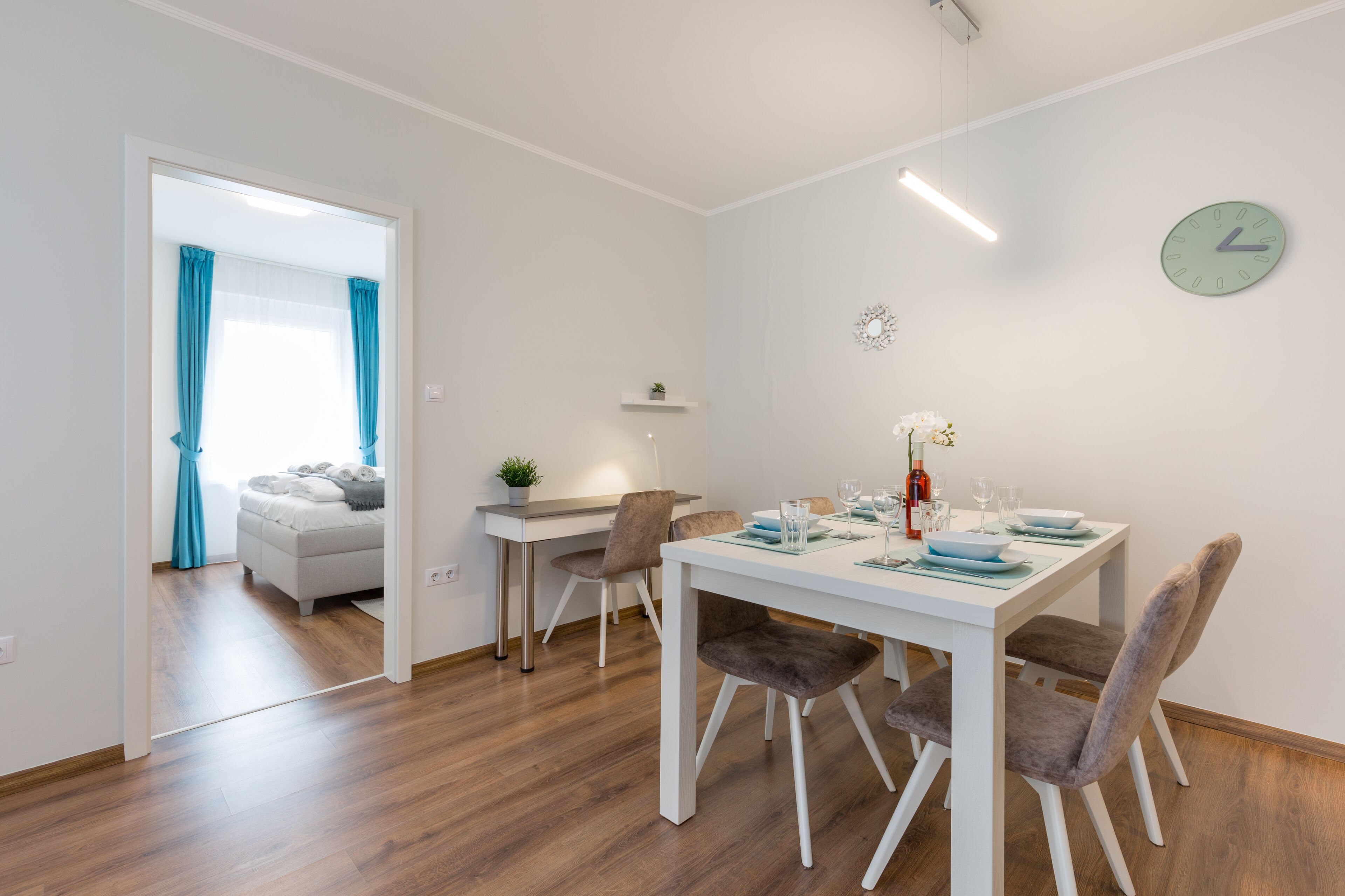 Una zona de menjador moderna amb una taula blanca, quatre cadires i un rellotge a la paret.