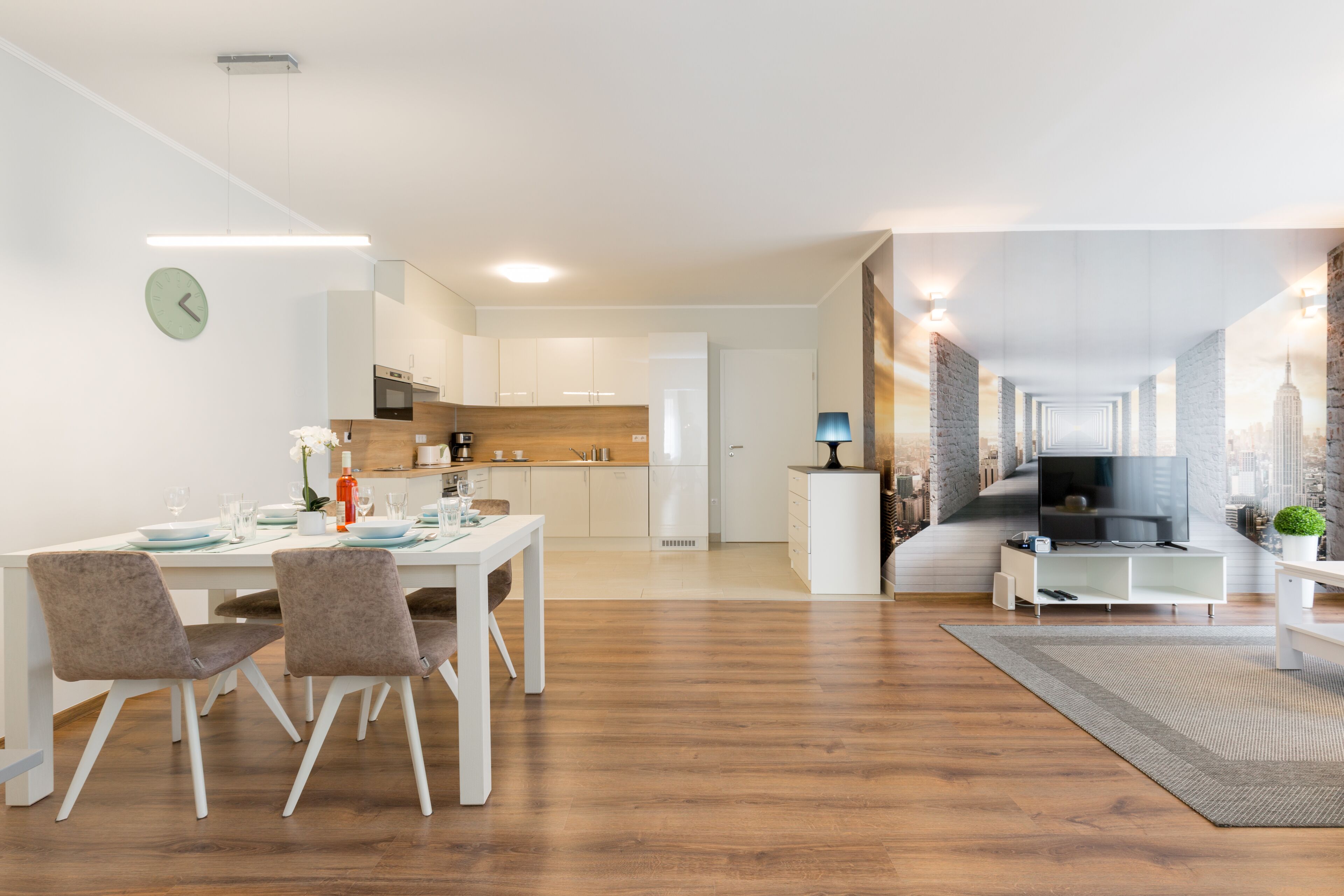 A modern apartment with a dining area, kitchen, living room, and a view of the cityscape.