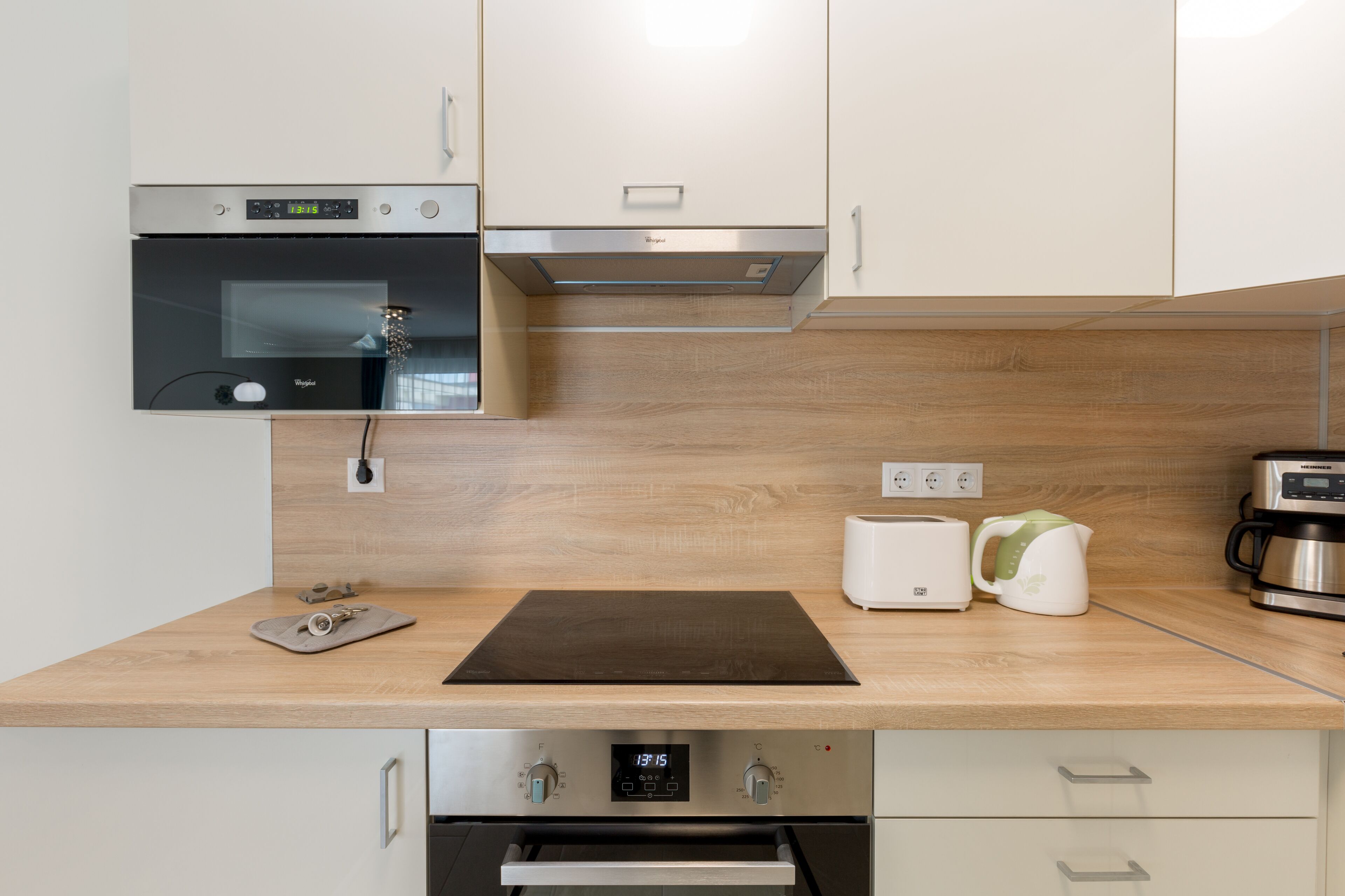 A modern kitchen with a built-in oven, a microwave, a stainless steel range hood, a wooden countertop, a kettle, and a coffee maker.