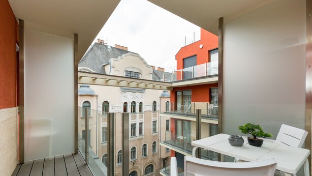 A balcony with a glass table and chairs, a potted plant, and a view of adjacent buildings. - Budapest Downtown Residence (Budapest)