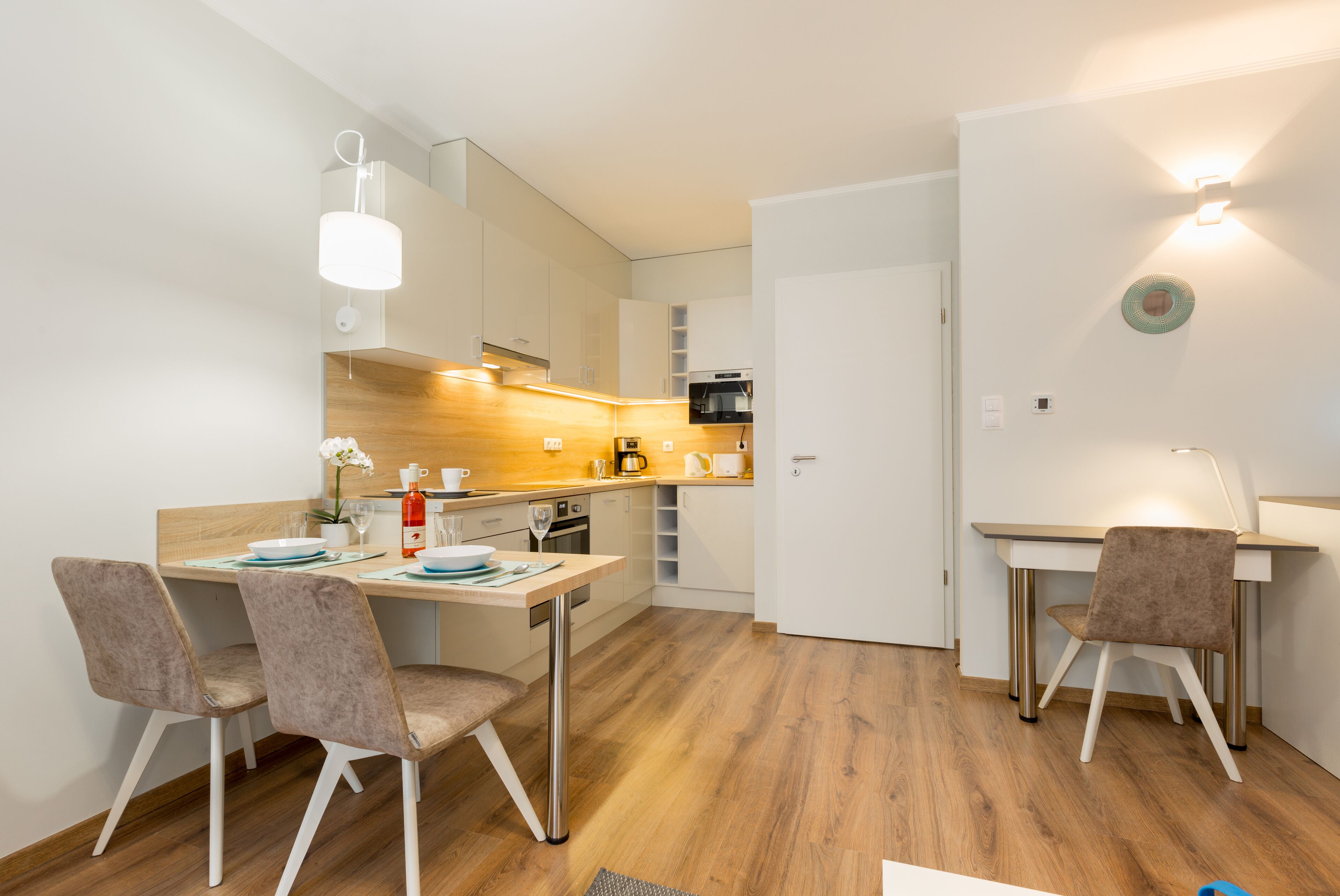 A modern kitchen with wooden flooring, white cabinets, and a dining area with two chairs and a table.