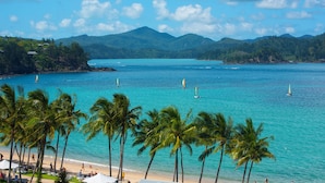 A beach with palm trees, clear blue water, and sailboats. - Frangipani 004, Hamilton Island (Hamilton Island)