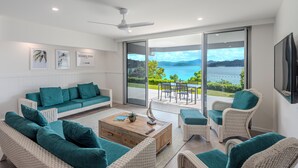 A modern living room with a large sliding glass door leading to a balcony with a scenic view. - Frangipani 004, Hamilton Island (Hamilton Island)