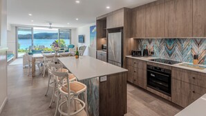 A modern kitchen with a large island, wooden cabinets, and a view of the sea. - Frangipani 004, Hamilton Island (Hamilton Island)