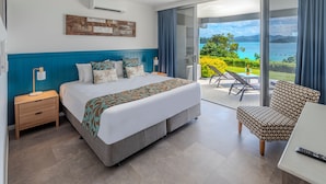 A modern hotel room with a large bed, a desk with a laptop, a chair, and a balcony with a view of the sea. - Frangipani 004, Hamilton Island (Hamilton Island)