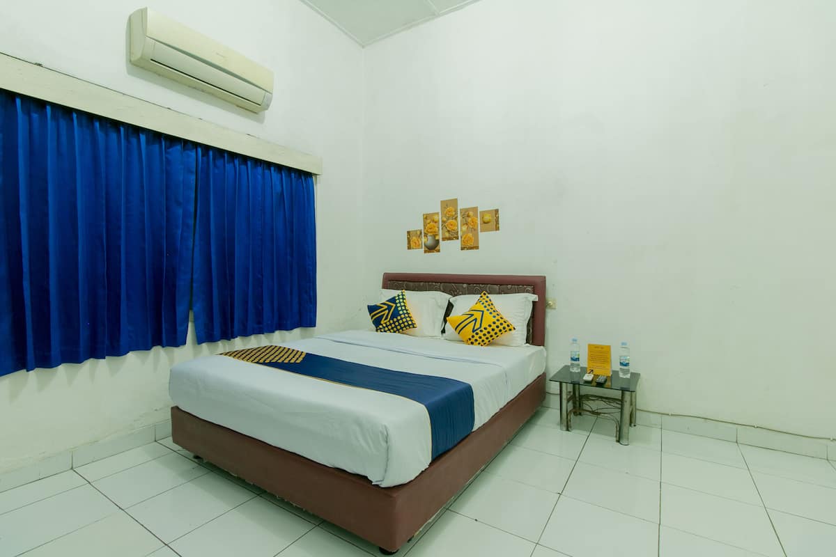 A bedroom with a bed, blue curtains, a wall-mounted air conditioner, a bedside table with a phone and water bottles, and a small wall decoration.