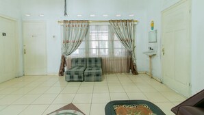 Ein Zimmer mit einer Couch, Vorhängen, einem Waschbecken und einer Wanduhr.