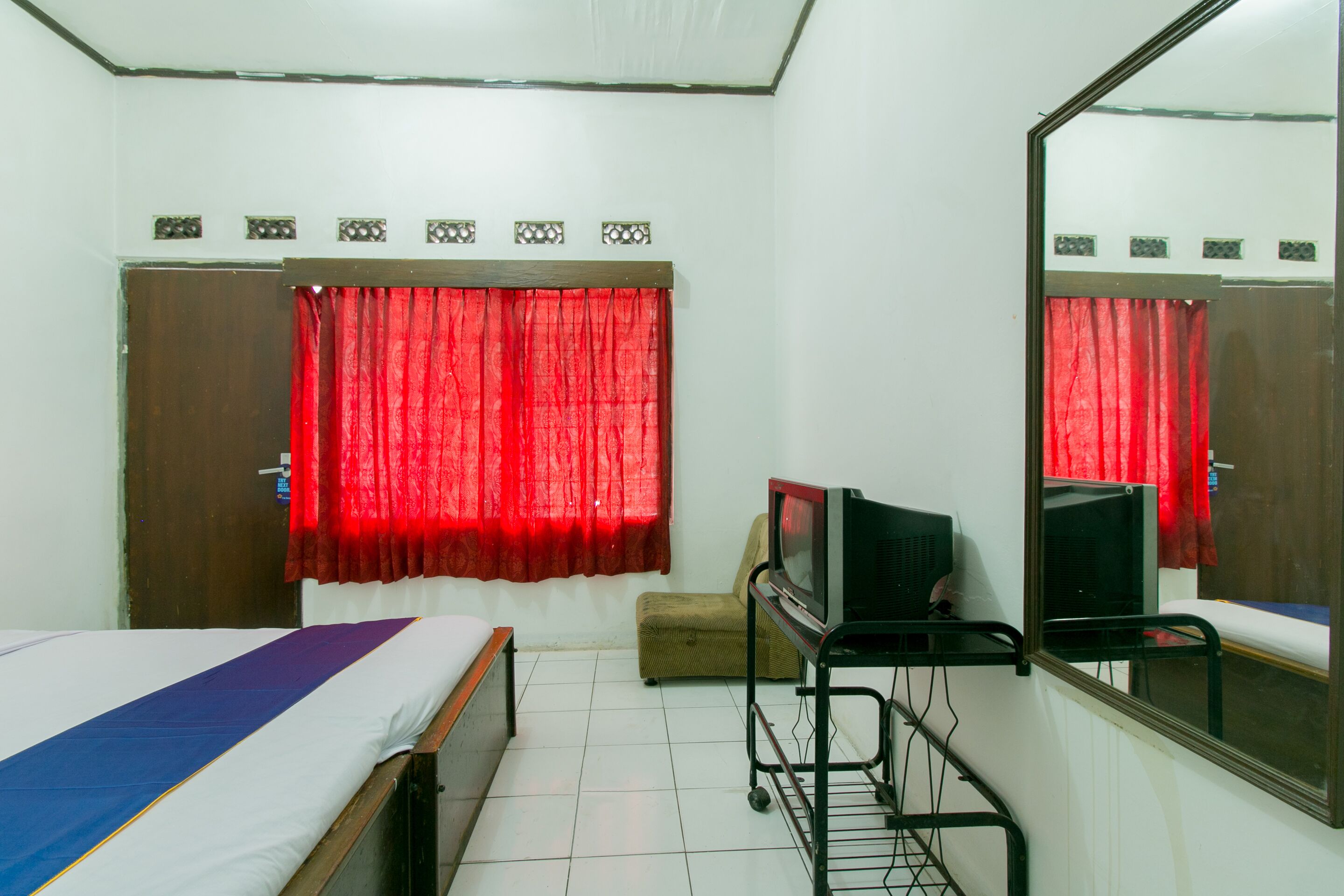 A room with a bed, a television on a stand, a small table, and a mirror on the wall.