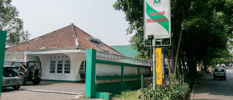 A hotel named Hotel Musistika with a green and white facade, a tiled roof, and a signboard.