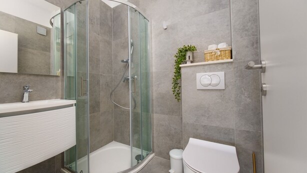 Un baño moderno con ducha de vidrio, lavamanos blanco y un inodoro.