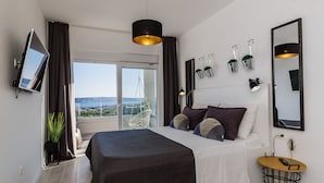 A modern bedroom with a large bed, a TV, a balcony with a view, and a small table with a lamp. - Villa Blue Wave , 8 bedrooms, 8 bathrooms,  2 swimming Pool, amazing Sea view  (Kaštel Stari)