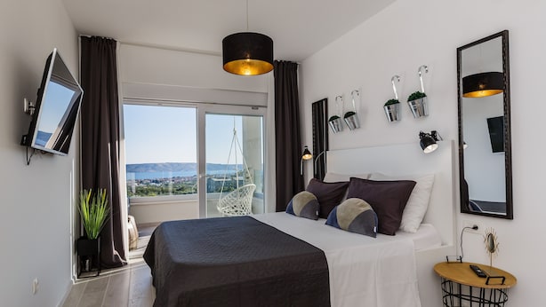 A modern bedroom with a large bed, a TV, a balcony with a view, and a small table with a lamp. - Villa Blue Wave , 8 bedrooms, 8 bathrooms,  2 swimming Pool, amazing Sea view  (Kaštel Stari)
