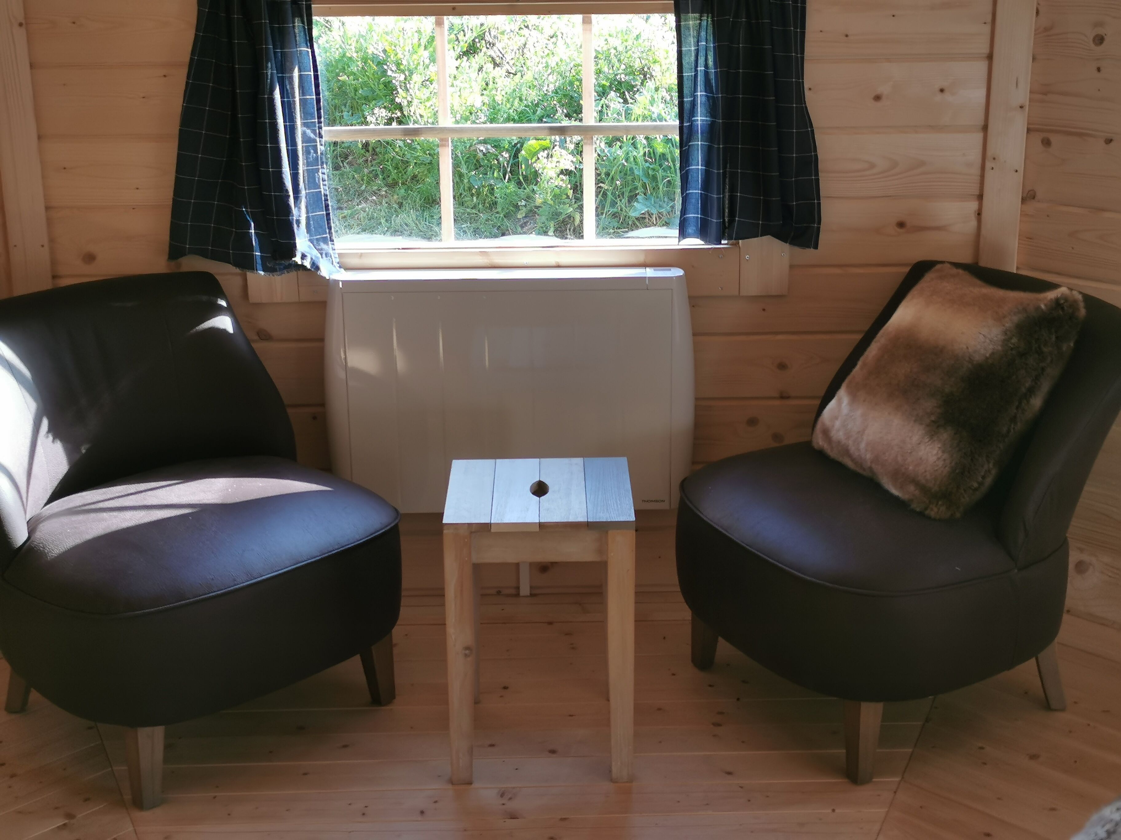 A cozy room with two black leather chairs, a small wooden table, and a window with curtains.