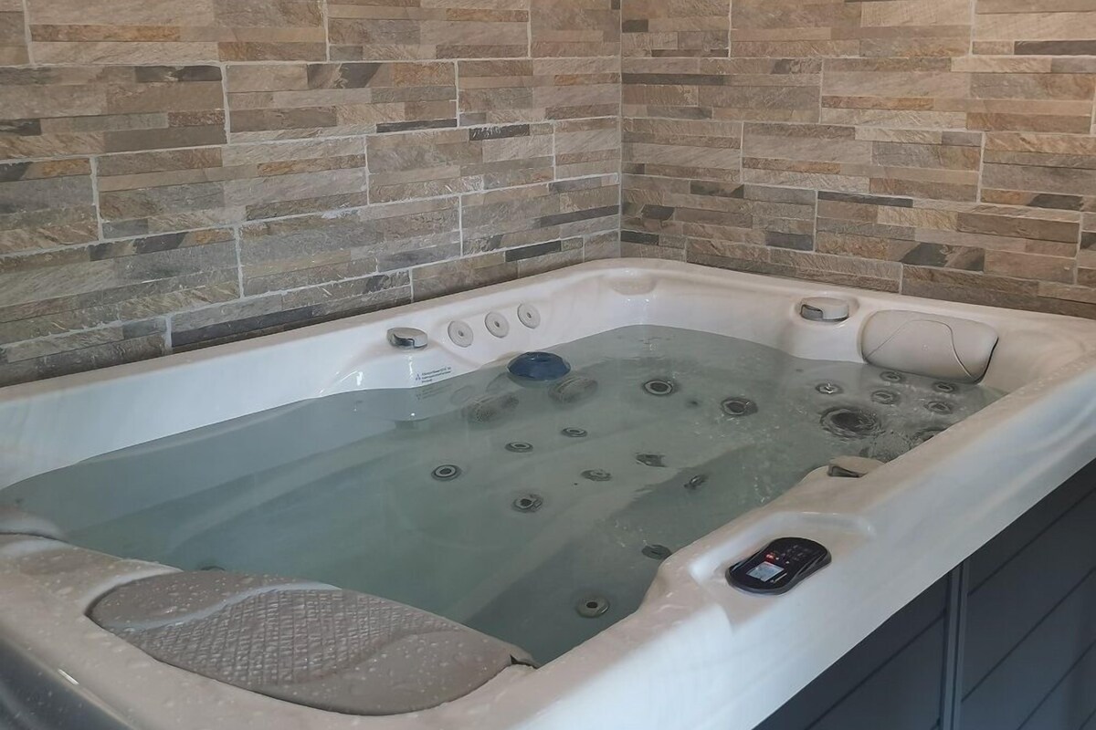 A hot tub with a control panel, set against a stone-tiled wall.