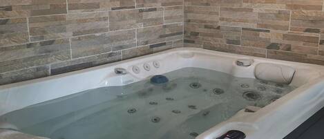 A hot tub with a control panel, set against a stone-tiled wall.