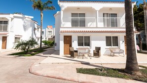 A white building with a balcony, a small garden, and a palm tree. - Fig Tree Z Holiday Villas DPS02- Two Bed Townhouse (Protaras)
