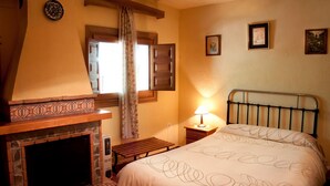 Une chambre à coucher avec une cheminée, un lit, une table de chevet et une fenêtre avec des rideaux.