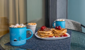 A breakfast setting with pancakes, strawberries, and a blue mug on a glass table.