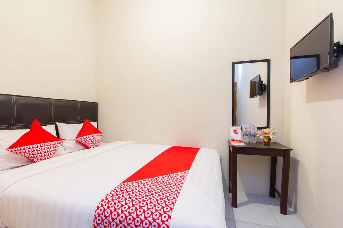 A hotel room with a bed, a bedside table with a mirror, and a flat-screen TV mounted on the wall.