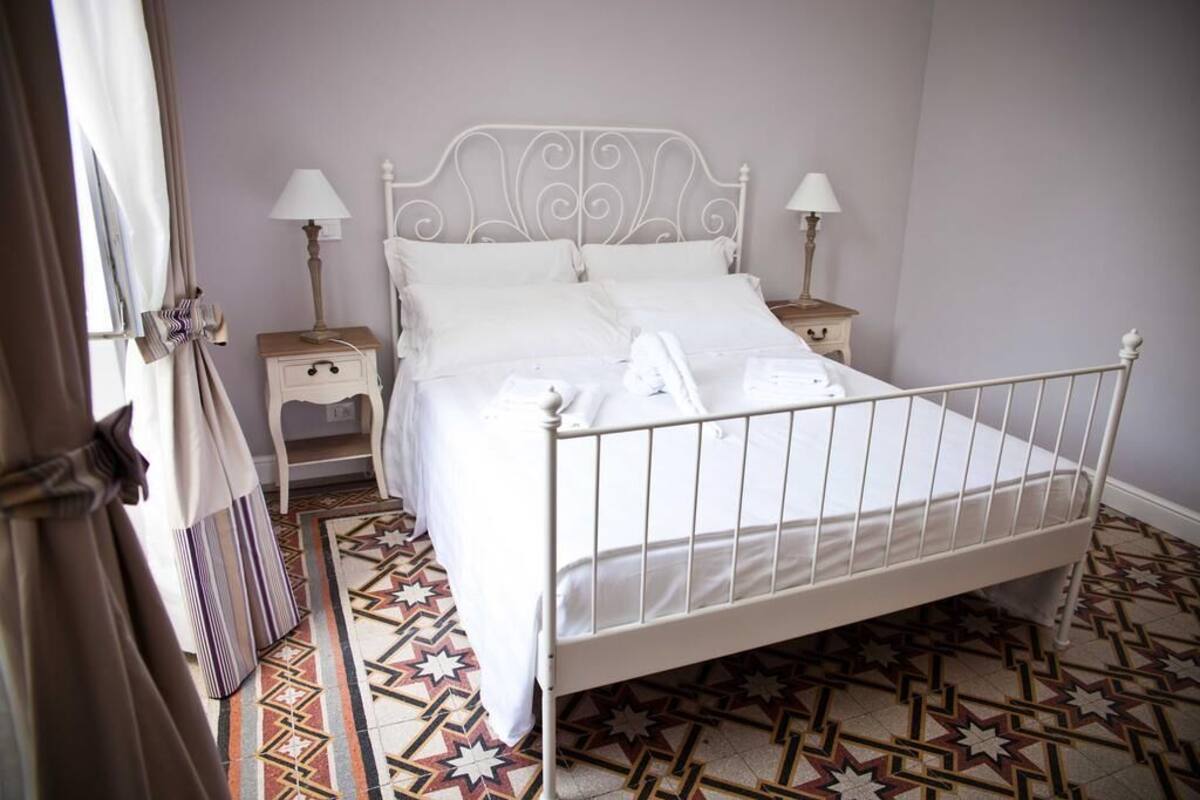 A neatly made bed with white linens, two bedside tables with lamps, and a patterned star-tiled floor.