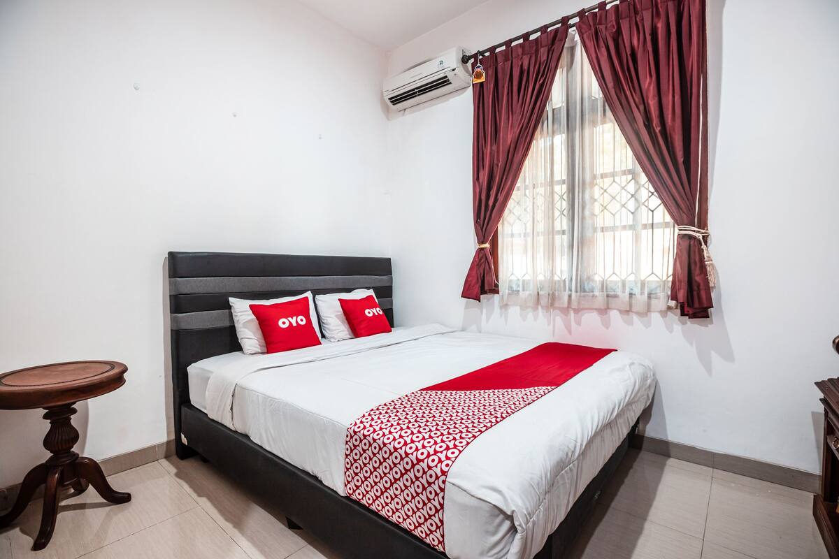 A neatly made bed with a patterned bedspread, a bedside table, and a window with curtains.