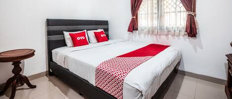 A neatly made bed with a patterned bedspread, a bedside table, and a window with curtains.