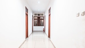 A hallway with a tiled floor, wooden doors, and a window with a metal grill. - OYO 1990 Kost Kuningan Executive Boading House Setiabudi (Jakarta)