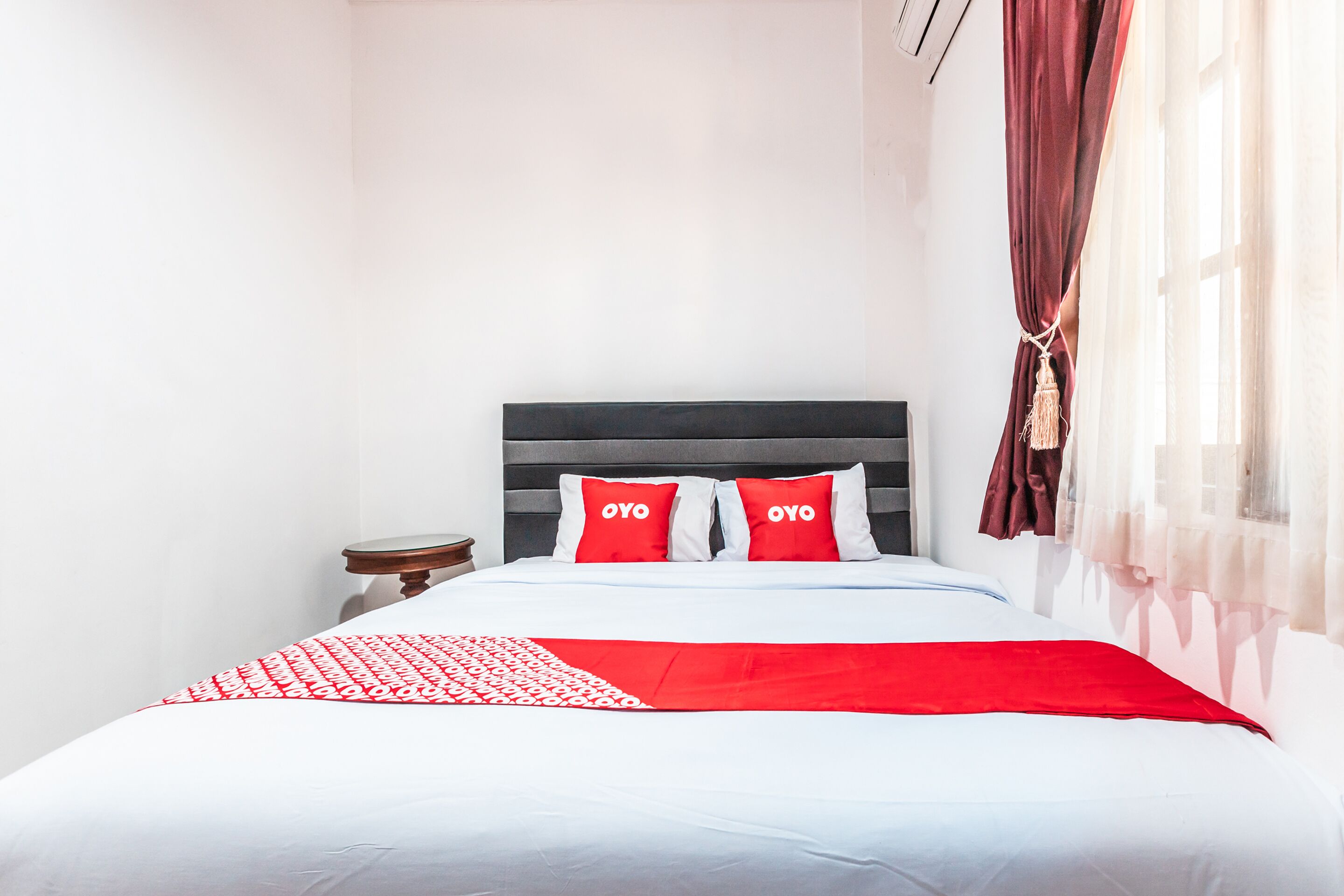 A neatly made bed with white and red bedding, a dark headboard, and a small bedside table.