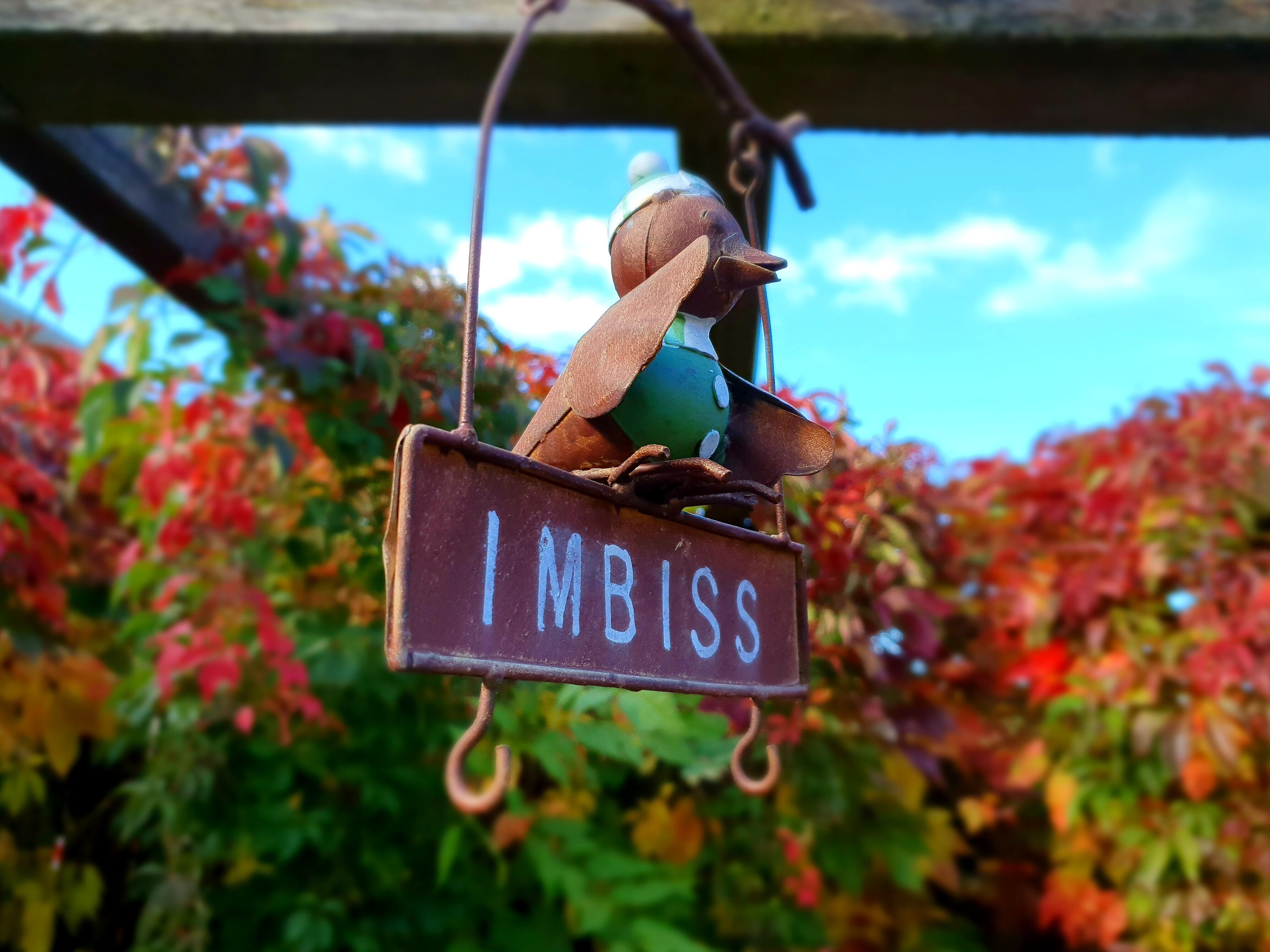 A rustic metal sign with the word "IMBISS" hanging from a hook.