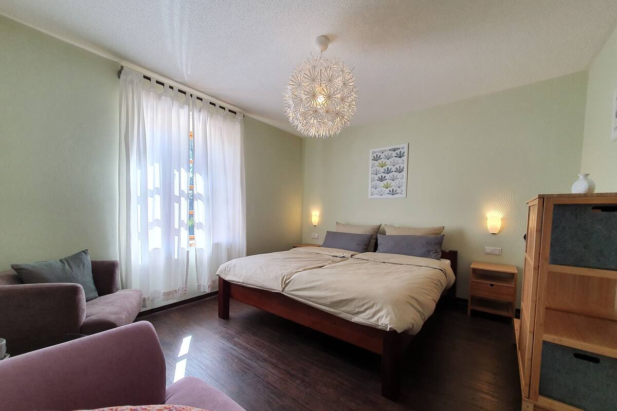Une chambre à coucher avec un grand lit, une table de chevet en bois, une chaise, un luminaire décoratif et une lampe fixée au mur.