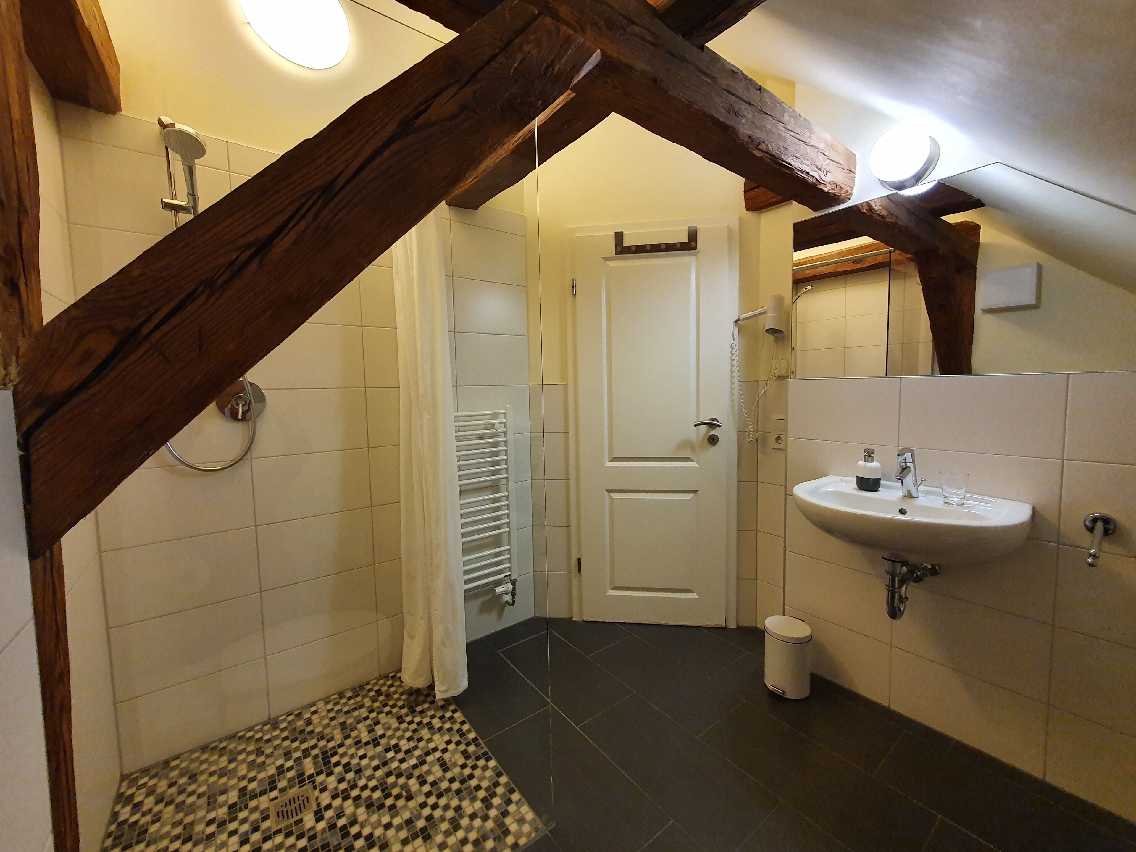 Une salle de bain avec un lavabo blanc, une douche et un sol carrelé.