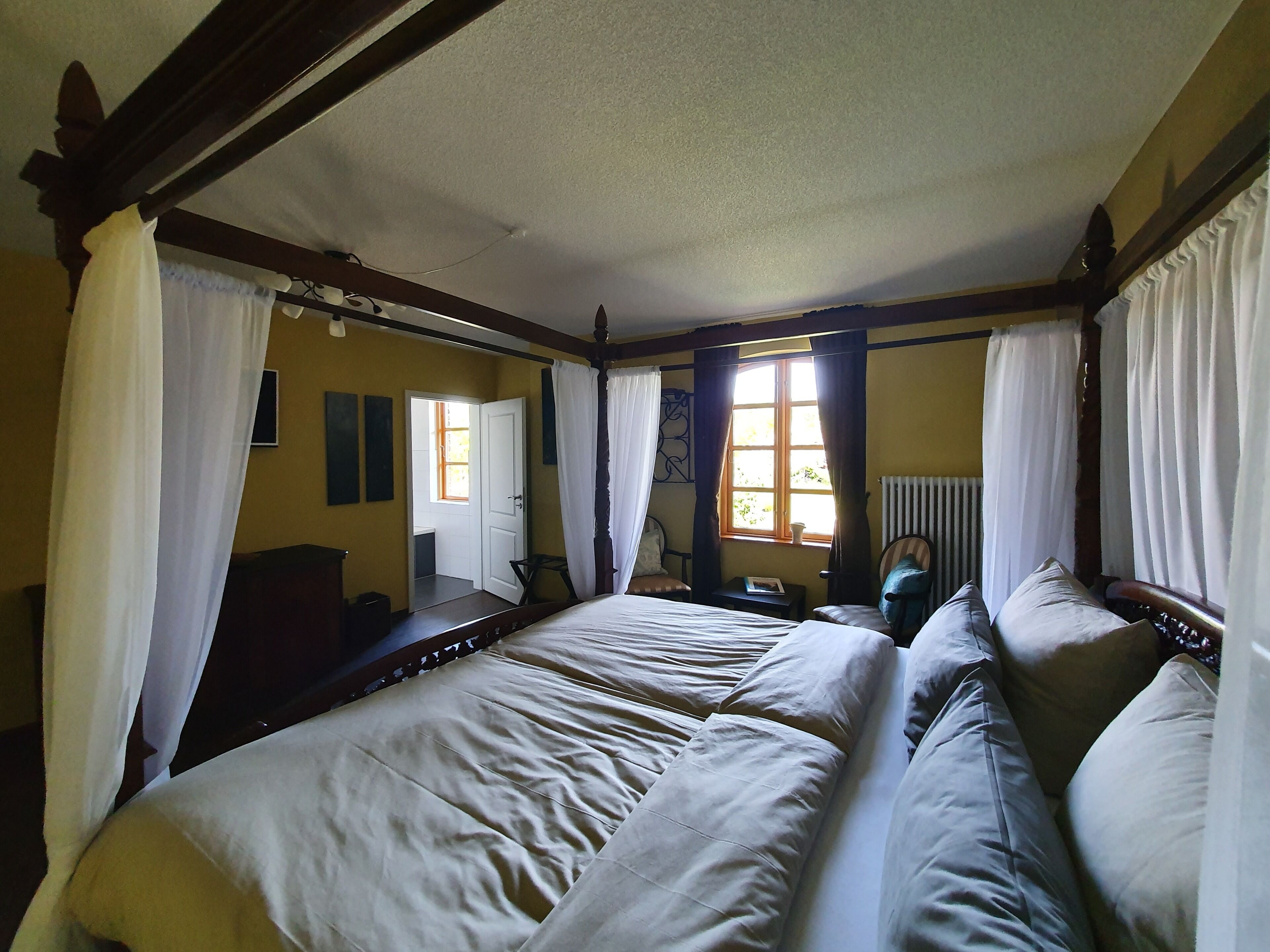 Ein Schlafzimmer mit einem großen Bett, einem Nachttisch, einem Sessel und einem Fenster mit Vorhängen.