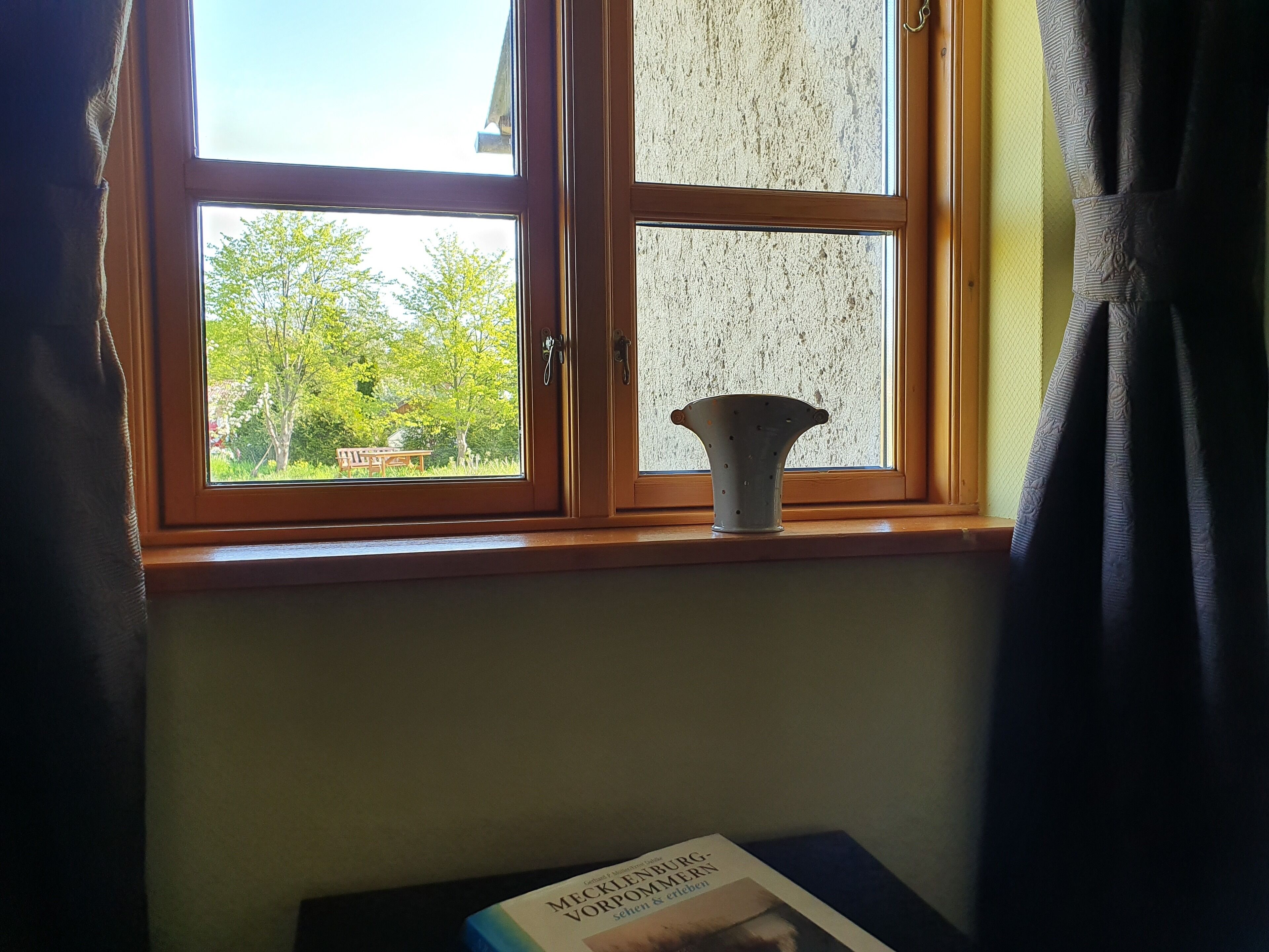 Janela com vista para vegetação e um banco do lado de fora.