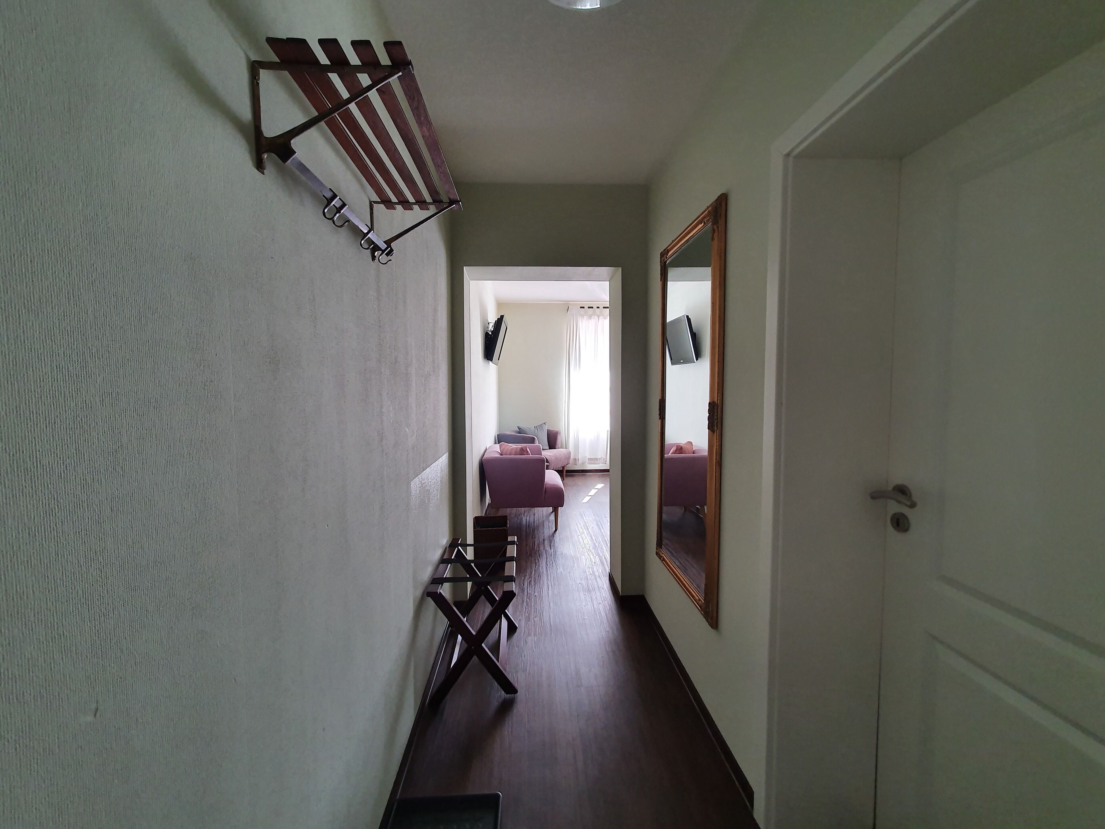 A hallway with a wooden bench, a wall-mounted drying rack, and a door leading to a living area with a couch and a TV.