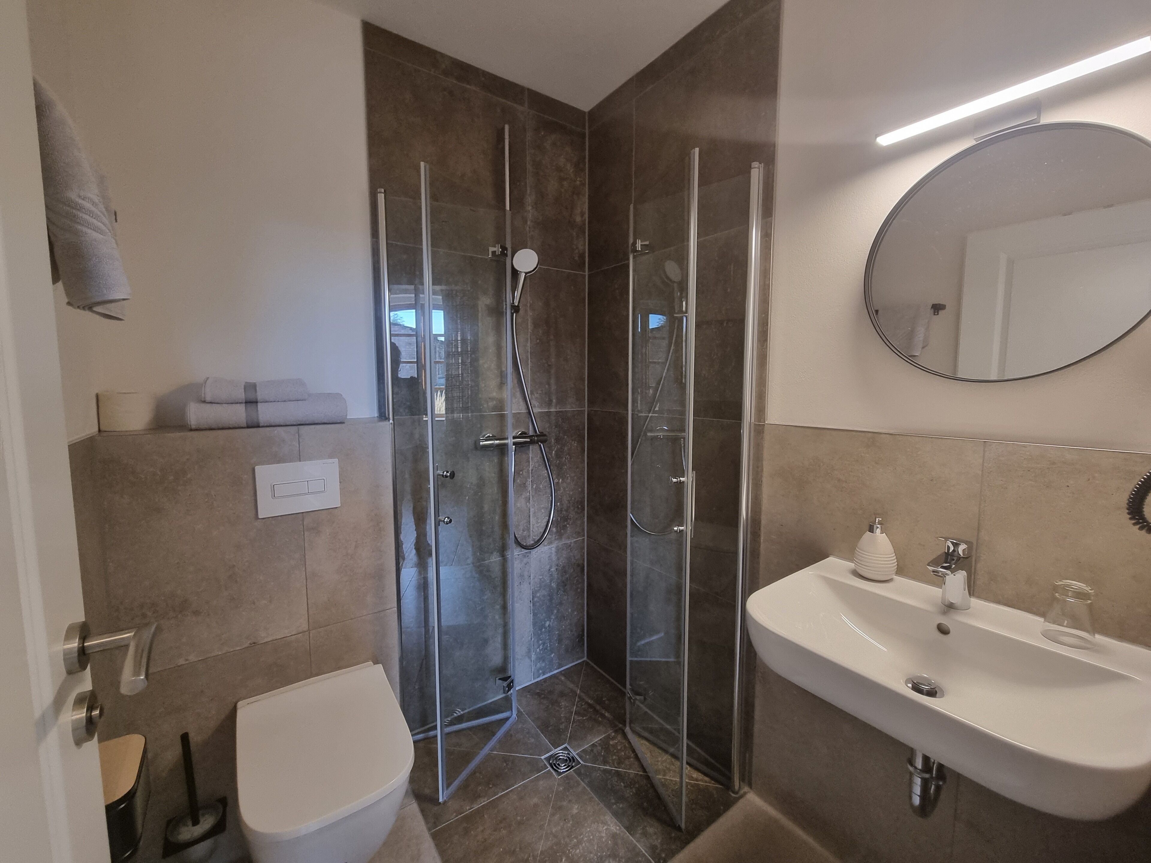 Ein modernes Badezimmer mit einer Duschkabine, einem weißen Waschbecken und einer Toilette.