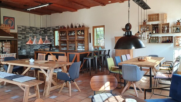 Een ruime eethoek met houten tafels en stoelen, een bar met flessenkasten, en een rustieke bakstenen muur.