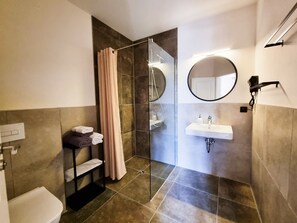 Un baño moderno con cabina de ducha de vidrio, un lavabo con espejo y un perchero con toallas dobladas.