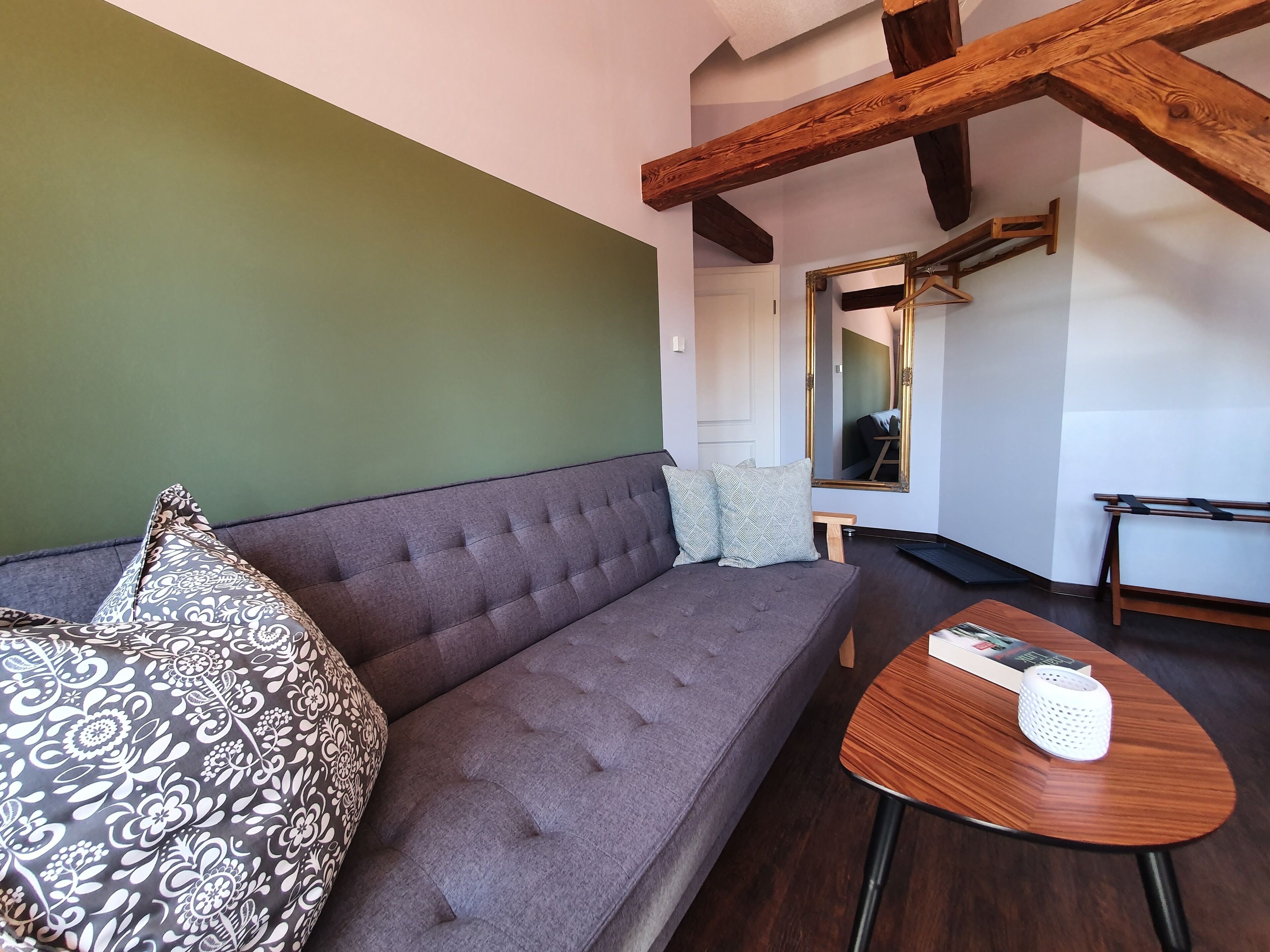 A modern living room with a grey sofa, patterned pillows, a small wooden table, and a mirror with a gold frame.