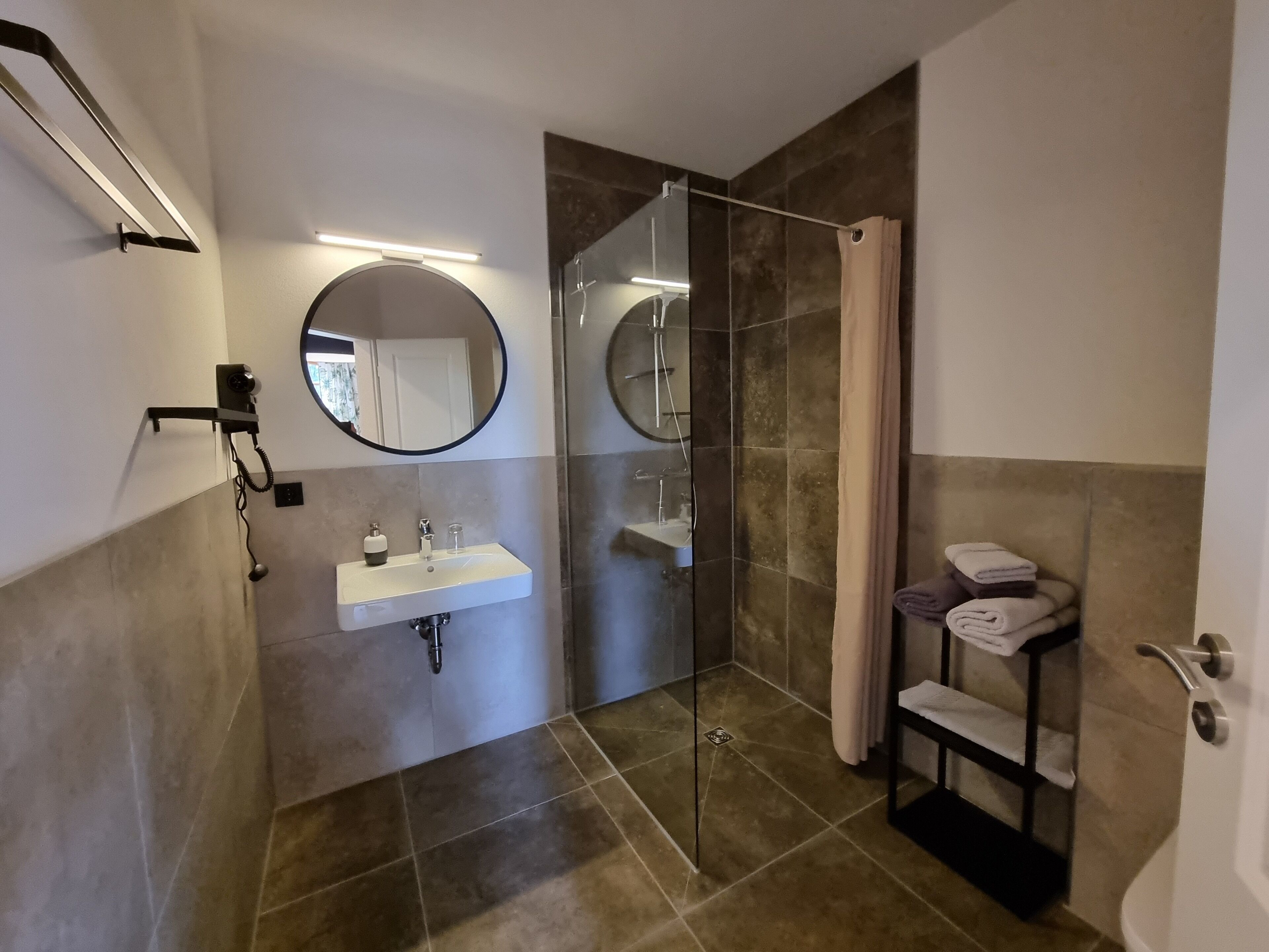 Un baño moderno con ducha envuelta en vidrio, un lavabo con espejo y un perchero con toallas.