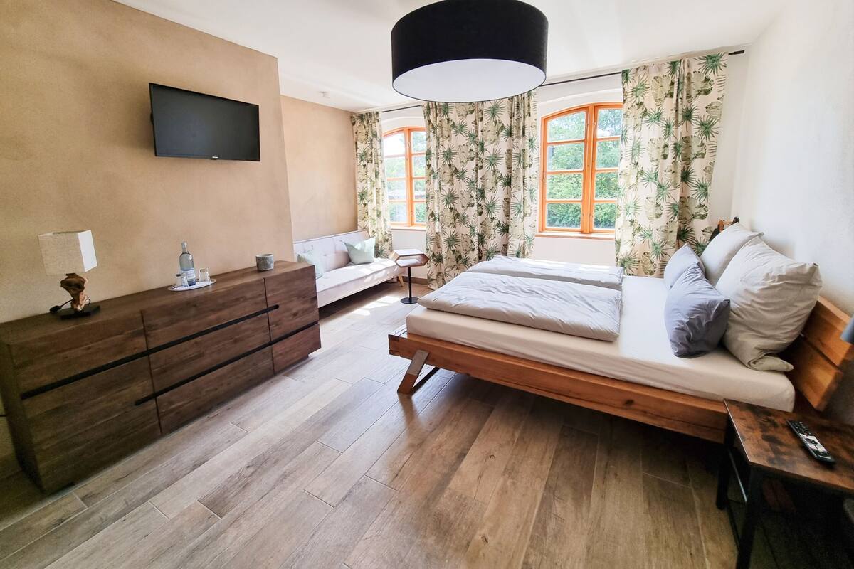 Une chambre à coucher avec un lit, une commode en bois, un téléviseur et une fenêtre avec des rideaux.