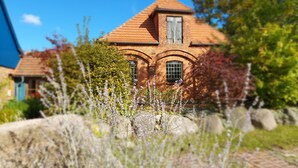 Een bakstenen huis met een pannendak, boogvensters en een tuin met verschillende planten.