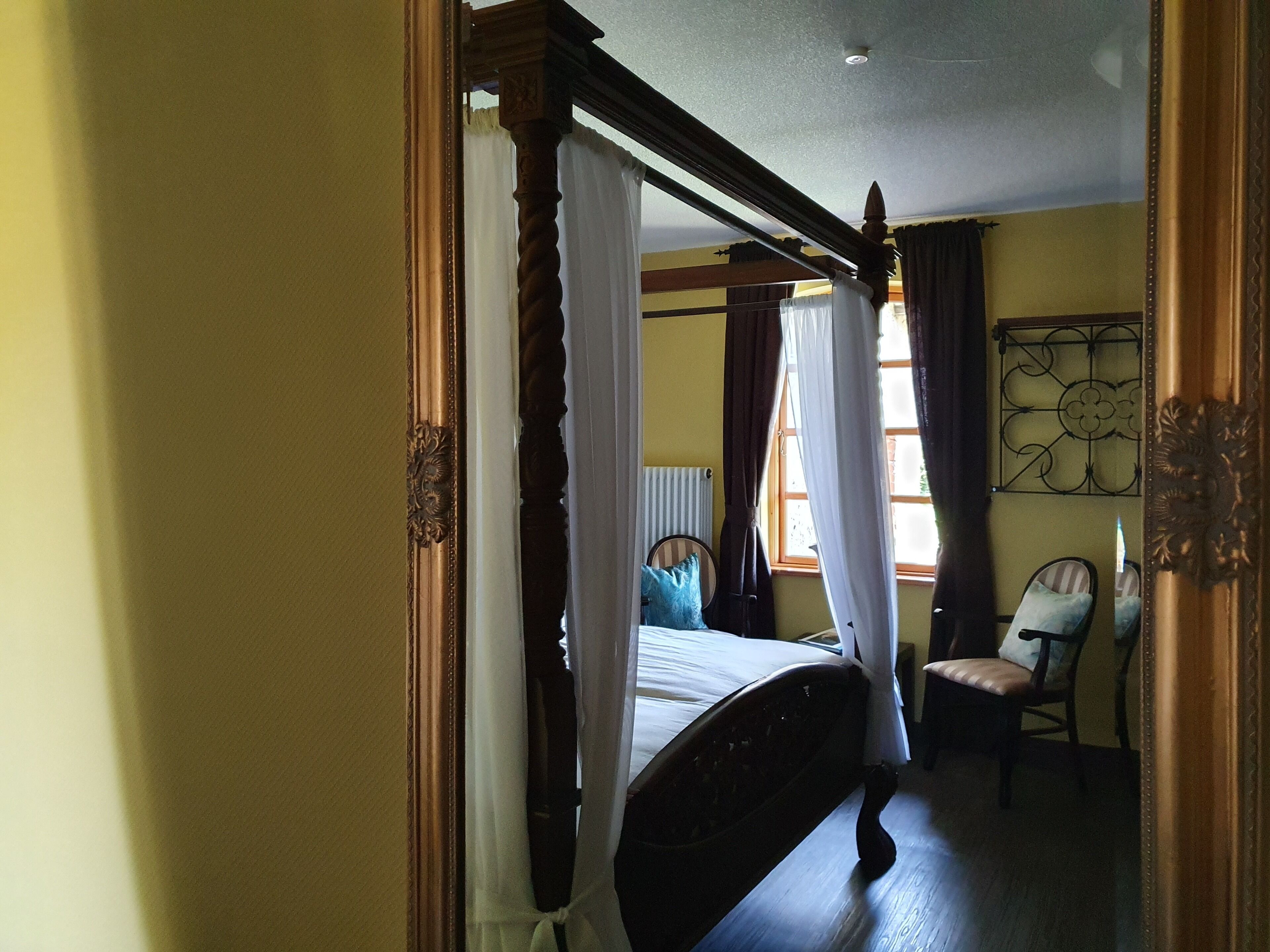 A bedroom with a four-poster bed, a chair, and a window with curtains.